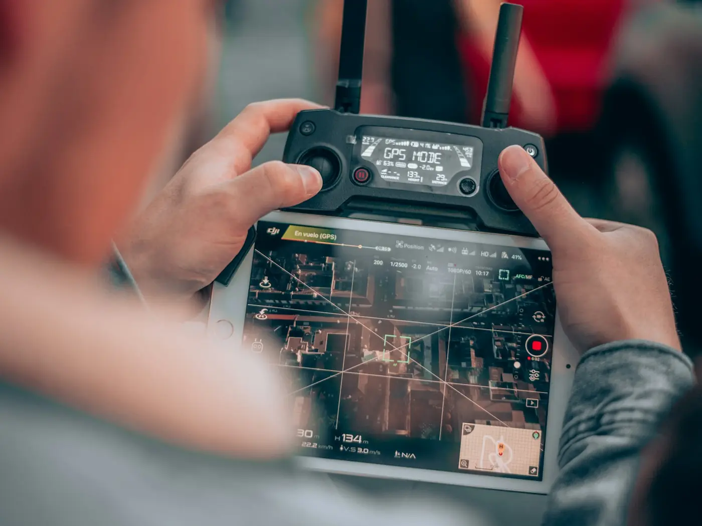 A pilot's hands on a drone controller with the live camera feed on screen