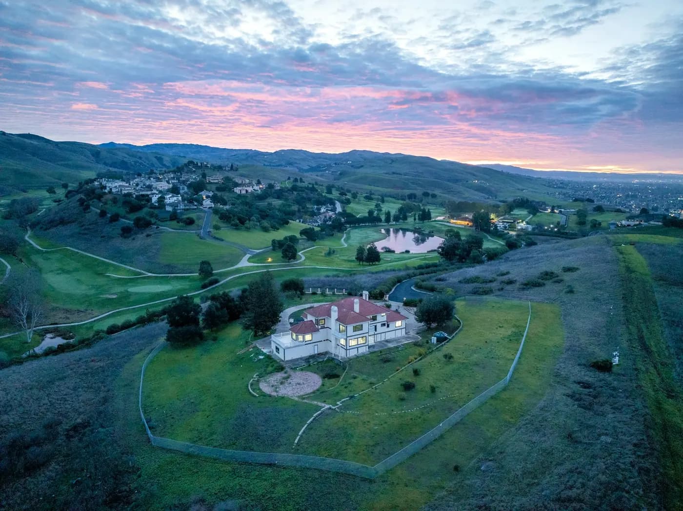 A house on a golf course under a pink sunset, seen from the air