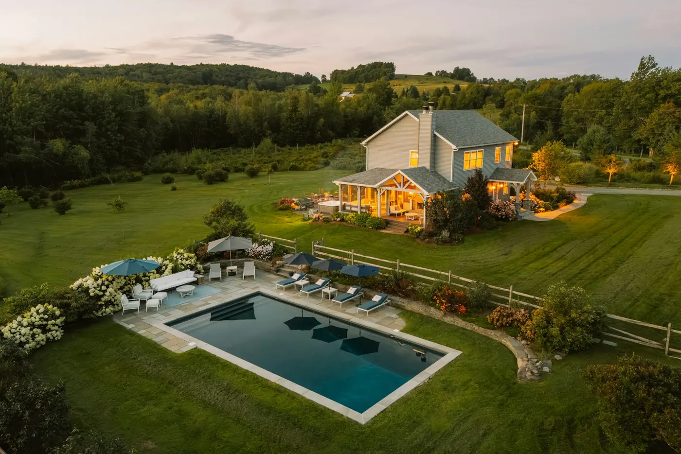 A house with a lit pool and lawn at dusk, seen from the air