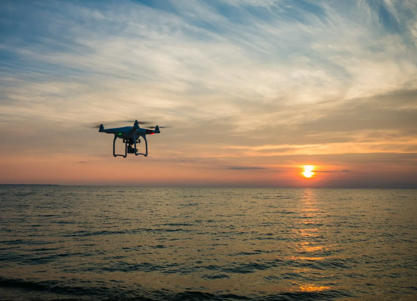 A drone flying over the sea at sunset