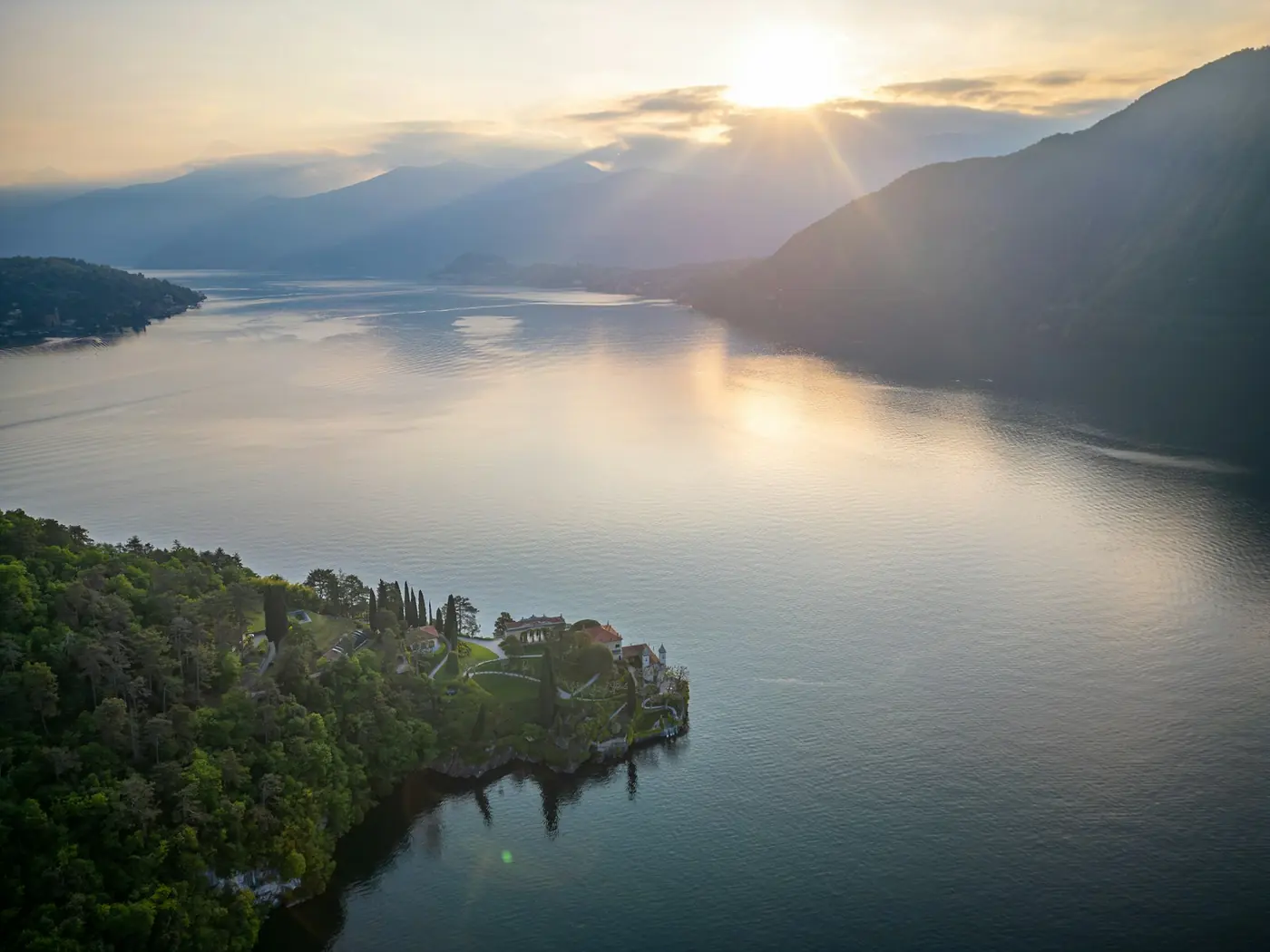 Sunbeams over a lake and a forested peninsula, seen from the air