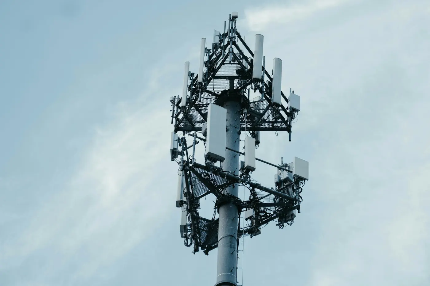 Cell tower with panel antennas against a pale sky