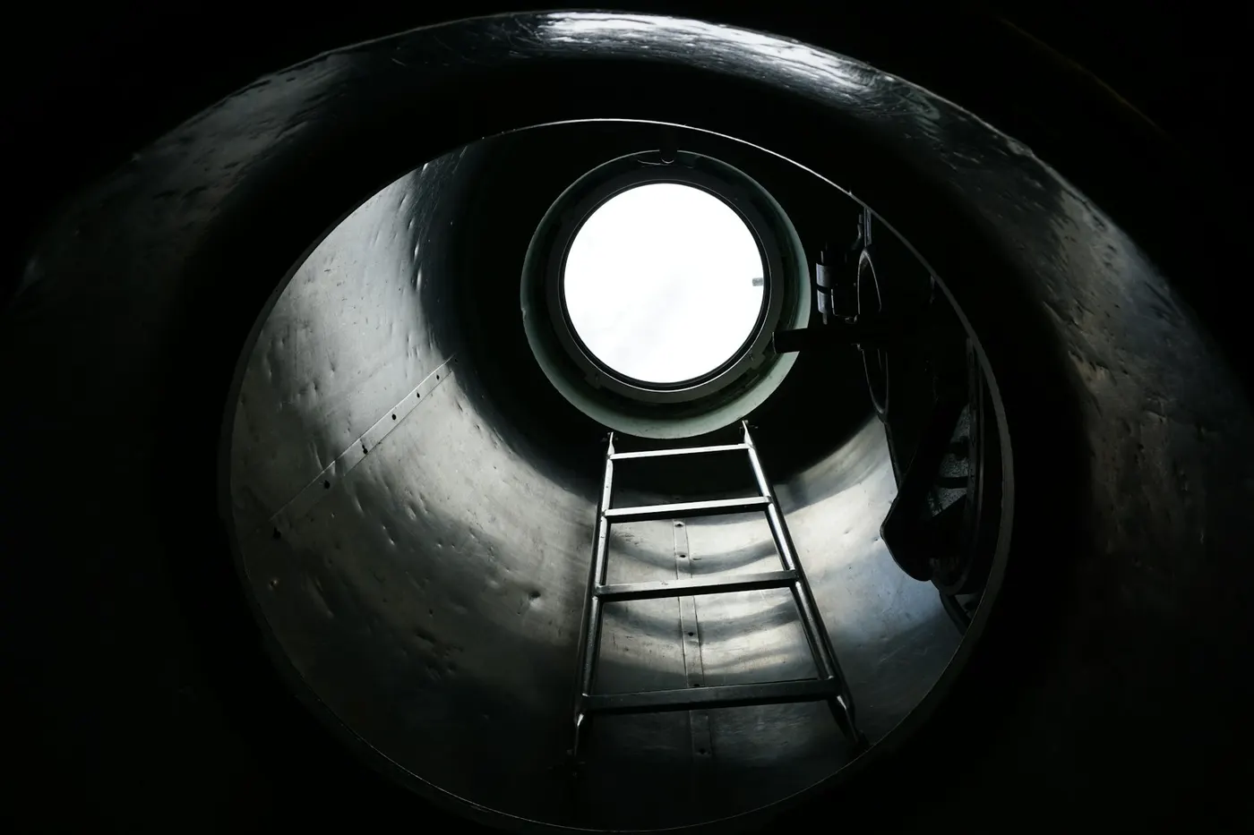 Looking up inside a steel tank toward a ladder and hatch