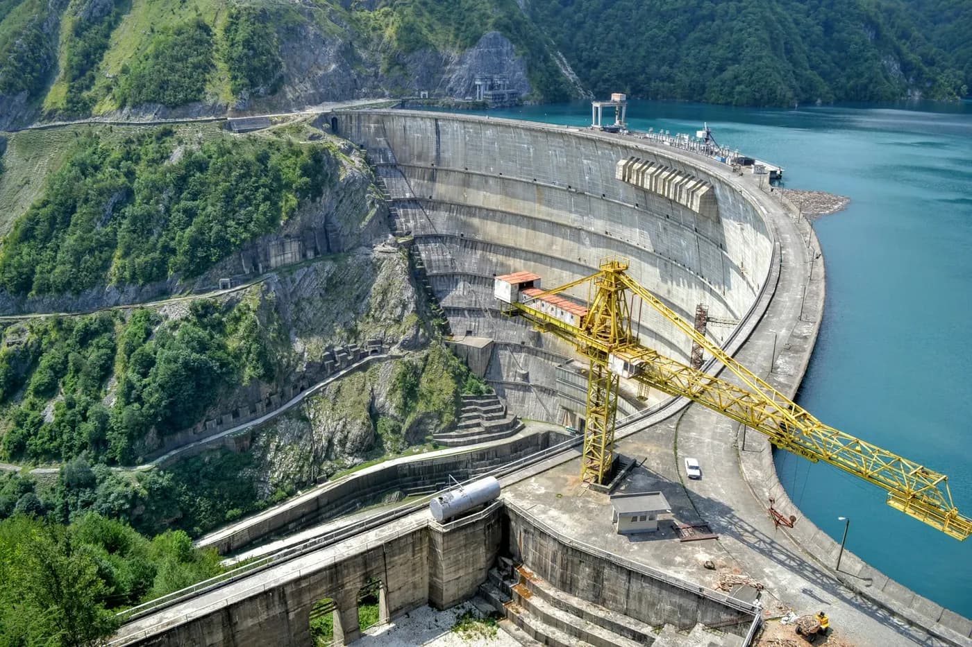 Aerial view of a curved concrete dam beside a crane