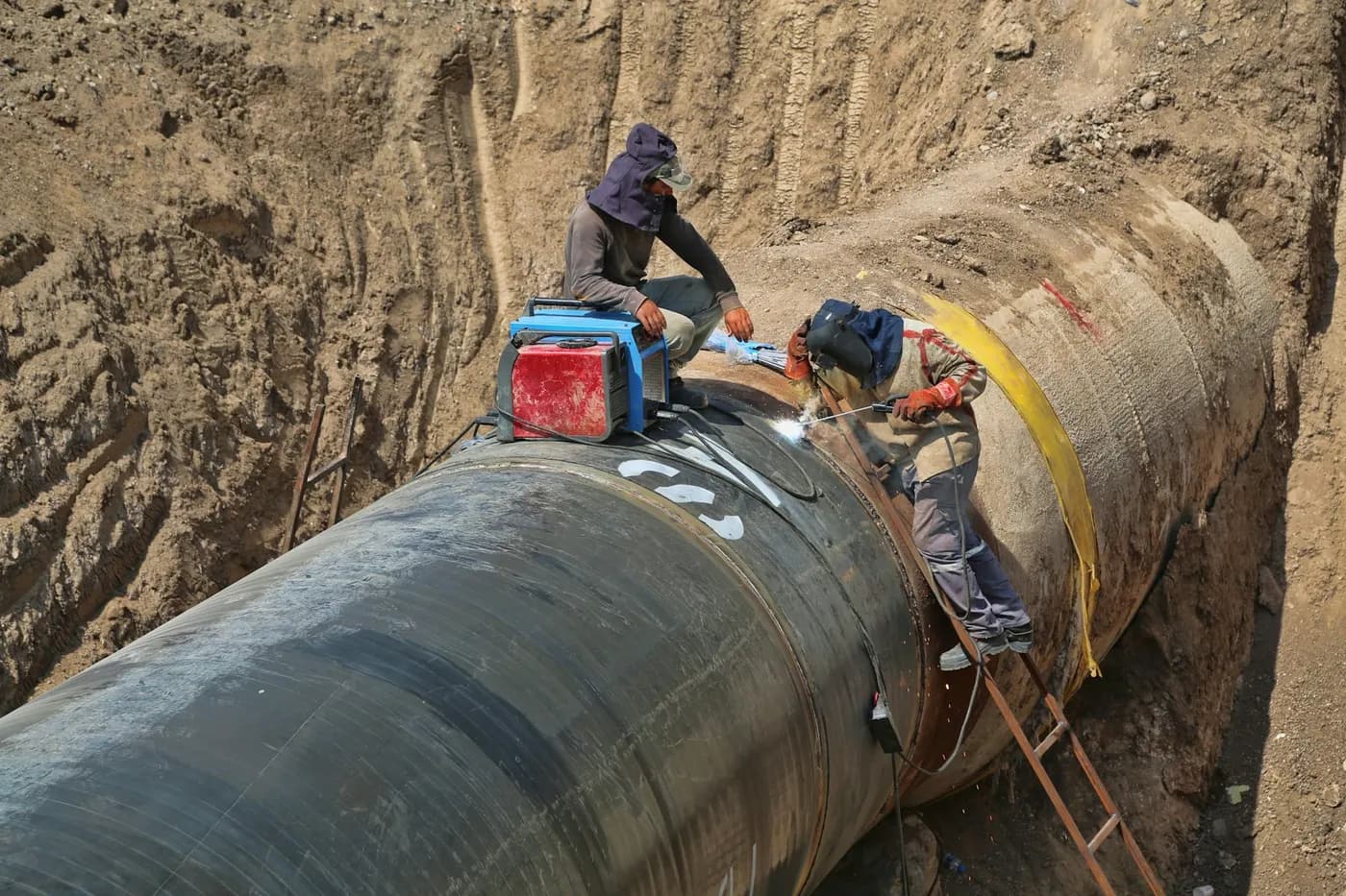 Workers on a large pipe in an excavated trench