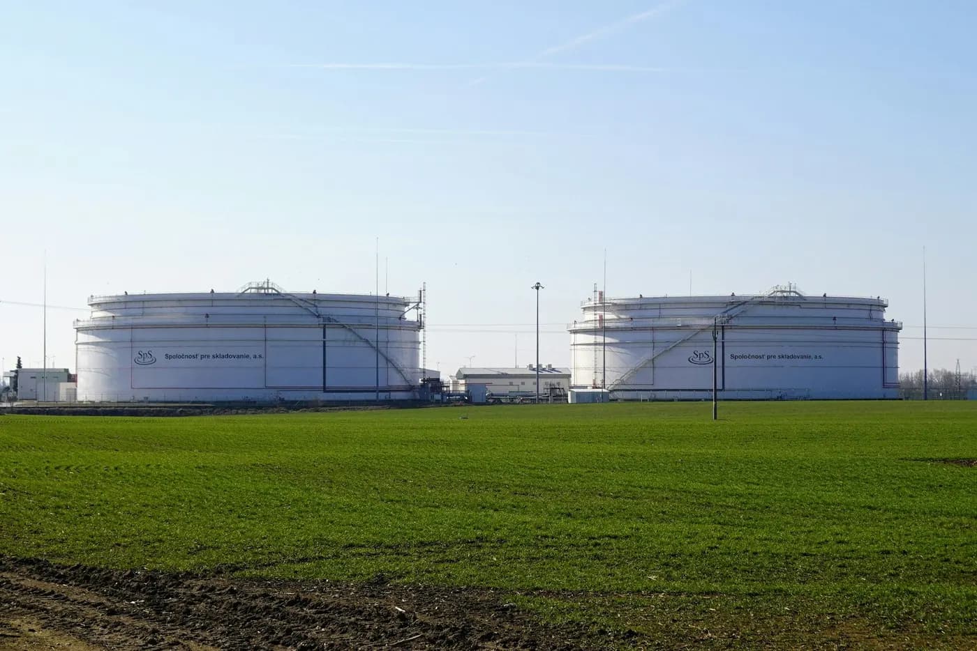 Two large white storage tanks beside a green field