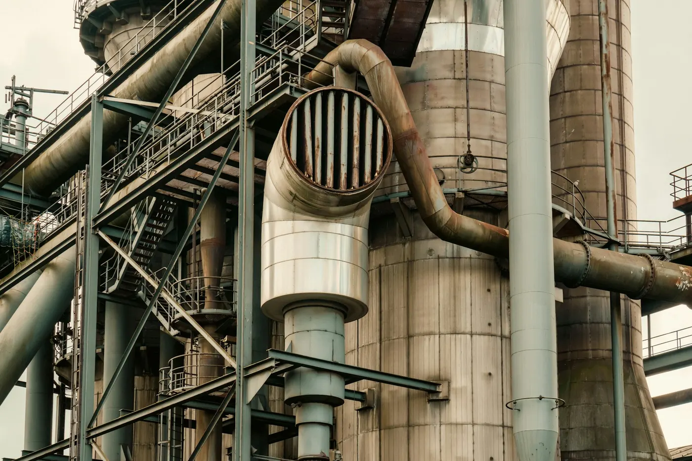Vedere de aproape a unor conducte industriale și a unui coș