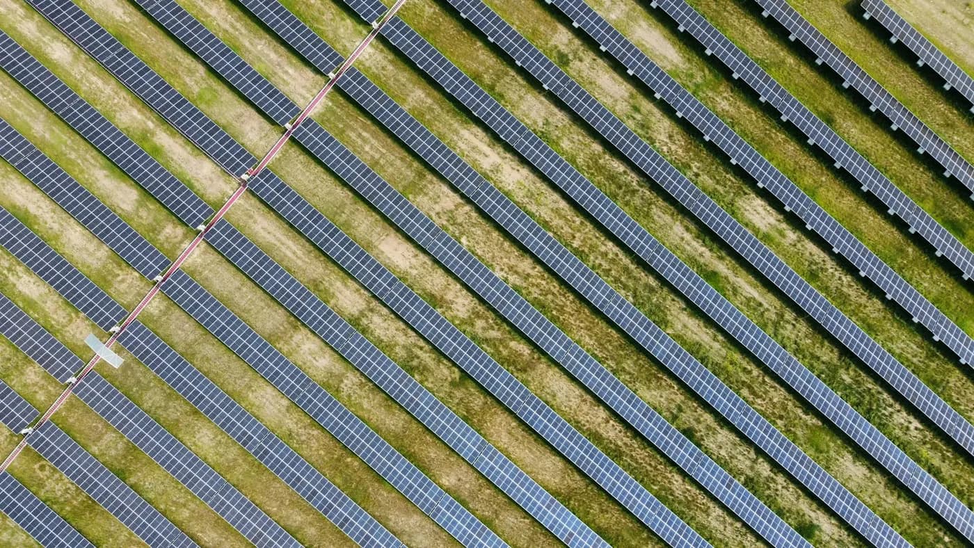 Rânduri diagonale de panouri solare pe un câmp, văzute din aer